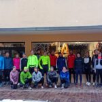 Eine Gruppe von 25 Personen in Sportkleidung steht vor einem Geschäft mit Schaufenster. Alle Teilnehmer haben verschiedene Oberteile in bunten Farben an und lächeln in die Kamera.