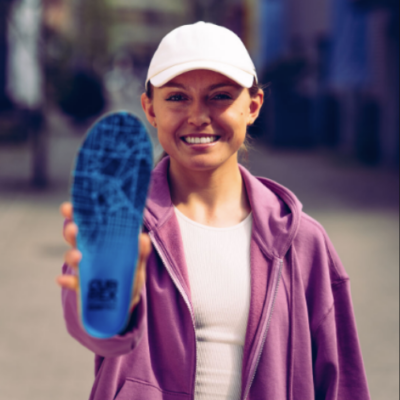 Die CURREX® RUNPRO™ dynamischen Einlegesohlen fürs Laufen in Blau, vorgezeigt von einer Person in lila Kapuzenjacke, bieten eine anatomische Unterstützung für Läufer.