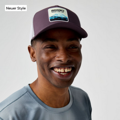 Brooks Running Cap - Trucker in lila mit Netzstoff-Rücken und Logo-Patch, dargestellt auf einem Mann, der auch ein sportliches Shirt trägt. Die Kappe ist leicht und atmungsaktiv, ideal für Laufaktivitäten.