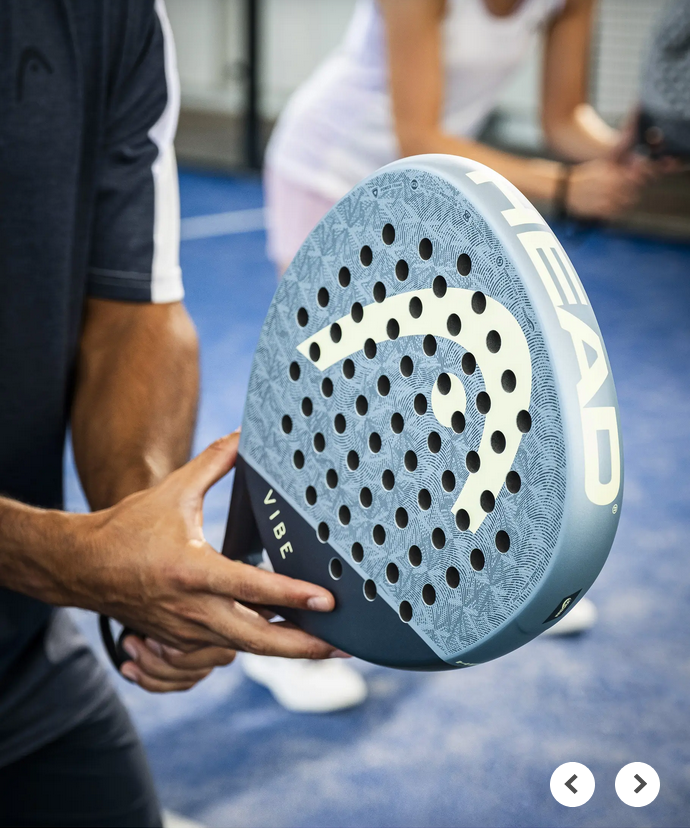 Padel Schläger Vibe von HEAD in blauer Farbe, mit einem charakteristischen Design und perforierter Oberfläche, gezeigt in der Hand eines Spielers auf dem Platz.